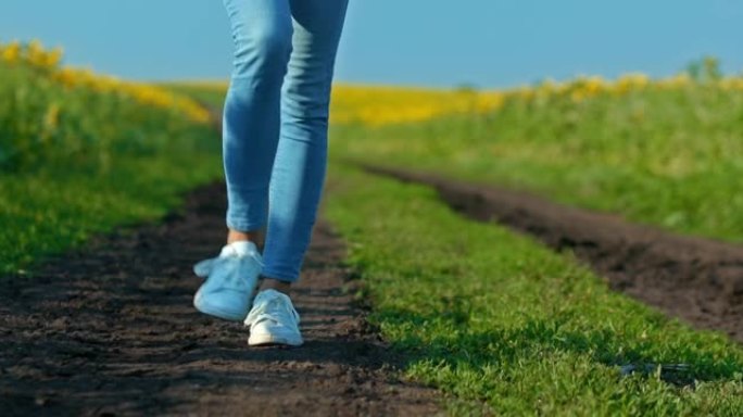 特写镜头，一个穿着白色运动鞋的女人的腿正沿着一条乡村道路行走。走在田野里的小路，脚踩着。底视图。4k