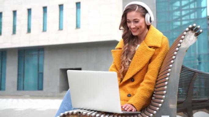 商务女性戴眼镜听音乐耳机户外坐凳使用笔记本电脑户外视频通话