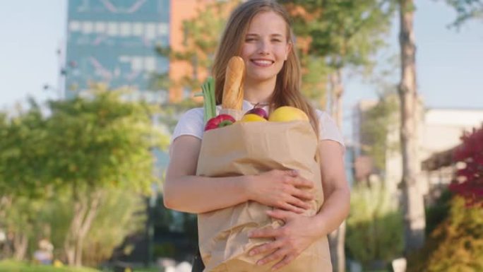 微笑的大美女在街中央购物后在镜头前摆姿势她拿着装满蔬菜和水果的生态袋