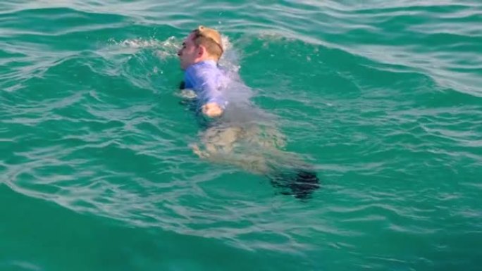 一个穿着衬衫，领带和袜子的有趣男人在阳光明媚的日子在海里游泳，然后潜入水下。慢动作，4k
