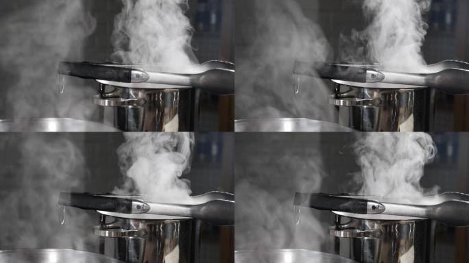 蒸汽或蒸汽云来自炉子上平底锅中的沸水。烹饪时从锅里蒸云。慢动作烹饪过程。蒸汽和白烟在黑暗的背景下升起
