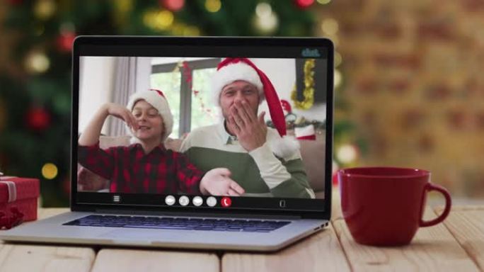 快乐的父亲和儿子在笔记本电脑上挥舞着视频，上面放着圣诞节装饰品和树