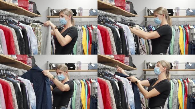 一名戴着防护口罩的中年妇女正在时装店为自己挑选衣服。折扣期间购物。女装的选择。