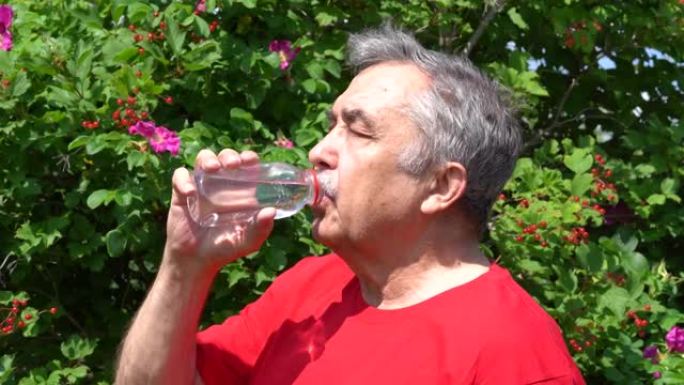 70岁老人的肖像在花园里拿着一瓶水，夏日。