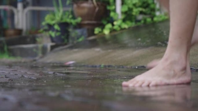 下雨活动后，赤脚在铺路水泥人行道上的水坑中慢慢踩踏，热带雨季，气候变化，环境问题，成年人玩水