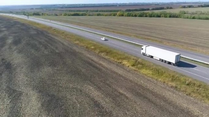 卡车在路上行驶，背景是田野。用卡车运输货物。卡车沿着农田顶部视图中间的道路行驶。