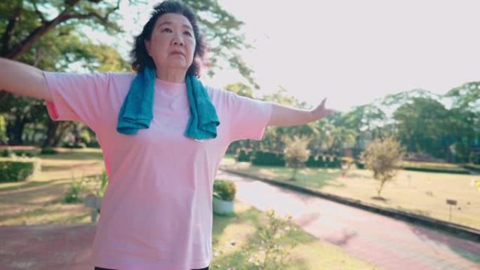穿着运动服的亚洲老人的肖像在绿色公园慢跑时伸展双臂，出汗锻炼，老年人的心血管护理，放松活动，行动不便