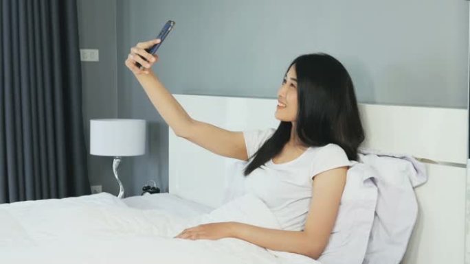 坐在智能手机上的年轻女子在卧室的床上自拍