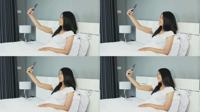 坐在智能手机上的年轻女子在卧室的床上自拍