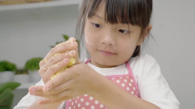 快乐的亚洲儿童在家里一起学习制作饼干，女孩在手里打谷面团。