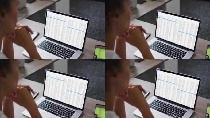 混血女人坐在办公桌前看着笔记本电脑屏幕上的编码数据处理