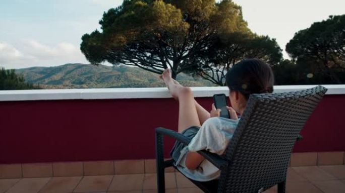 年轻女子在度假时在阳台上发冷，并使用智能手机发短信