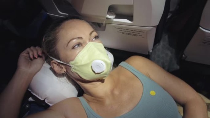 女人戴着防护医用口罩在飞机上旅行。女孩游客在带呼吸器的飞机上，感觉不好，睡觉。