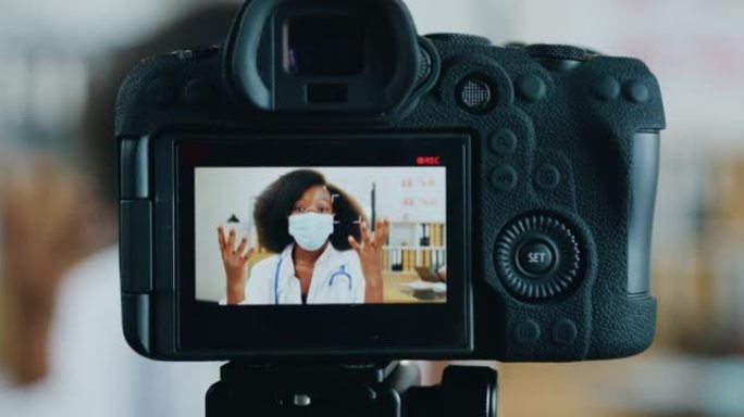 摄像机拍摄美丽自信友好的黑皮肤女性医生的面膜，从医疗办公室的摄像机上流出