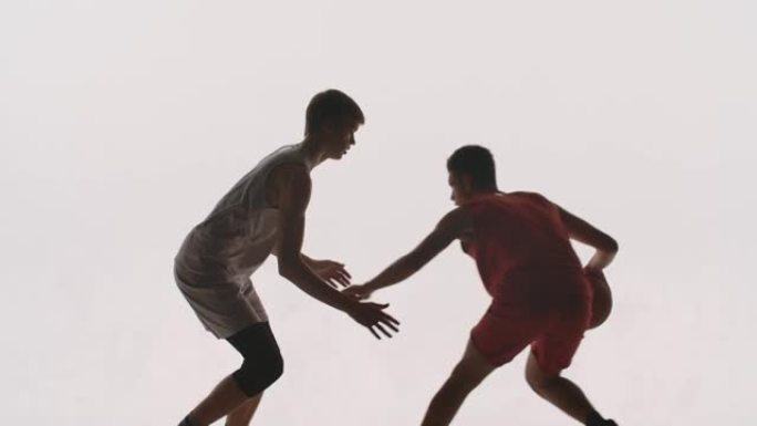 两个运动员的轮廓篮球运动员练习进攻和防守技巧。穿着运动服的高大对手在白色工作室背景下参加篮球比赛。慢