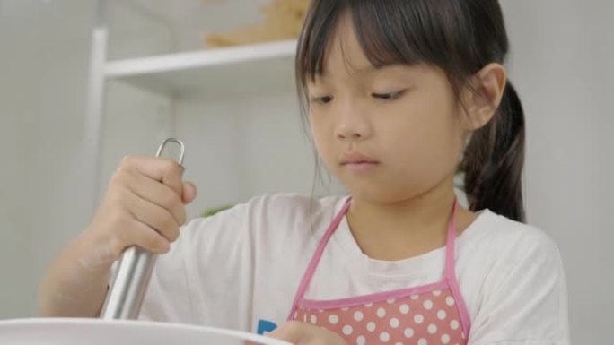 快乐的亚洲孩子在家里学习做饼干，女孩在搅拌碗里搅拌面粉。