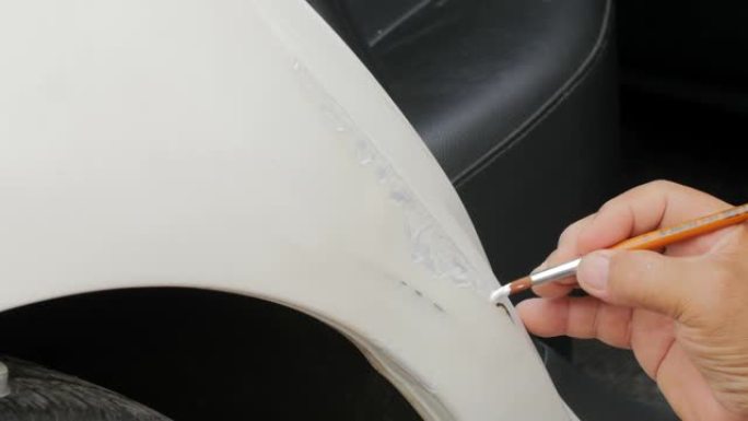 手工特写-一名男子在汽车油漆店用白色油漆覆盖后门线上的划痕。