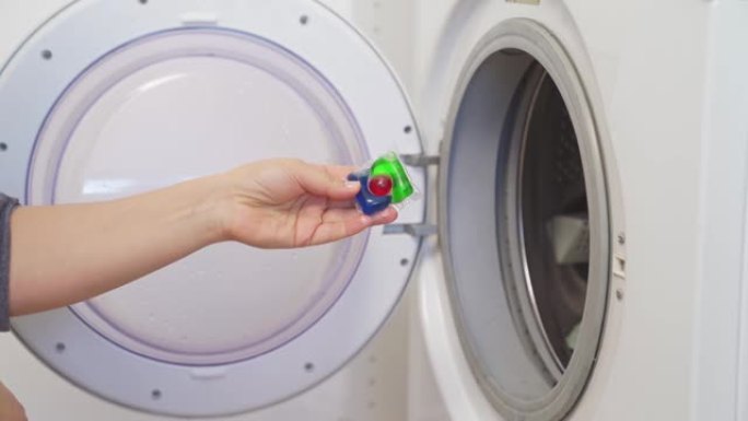 一个女人把装有洗衣粉的胶囊放在洗衣机里。