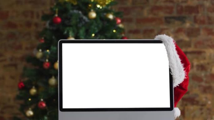 圣诞老人帽子挂在电脑显示器上，屏幕上有复印空间，有圣诞装饰品和树