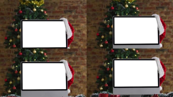 圣诞老人帽子挂在电脑显示器上，屏幕上有复印空间，有圣诞装饰品和树