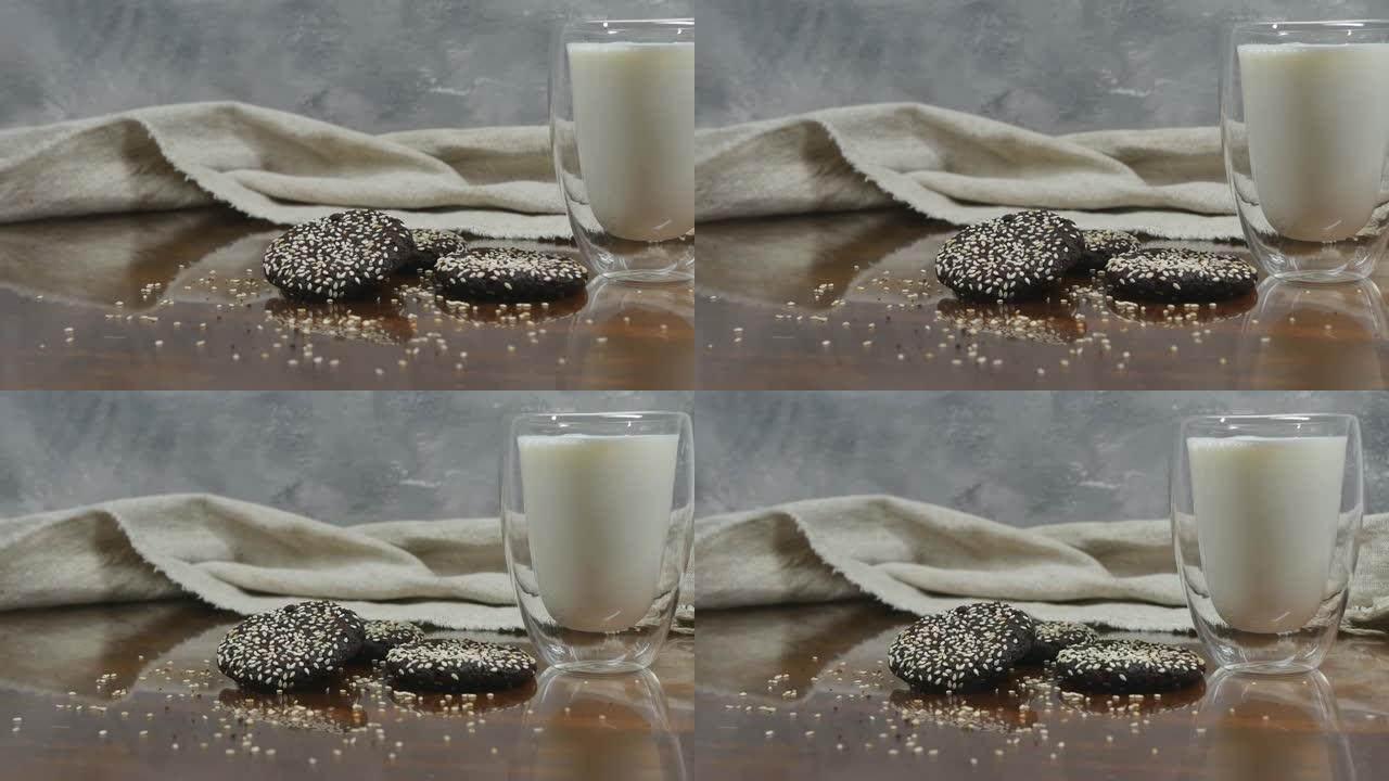 一杯牛奶旁边的桌子上放着芝麻巧克力饼干。桌子上的灰色背景和粗麻布。多莉射击