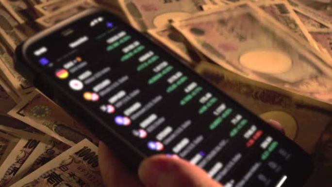 桌子上堆满了日元钞票，一只手操作着显示市场价格的智能手机。