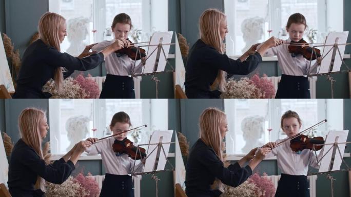年轻的女老师教小女孩如何在拉小提琴时正确握住弓