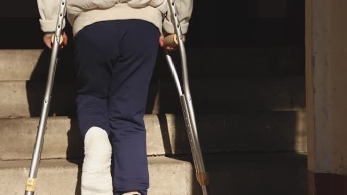 孩子拄着拐杖爬楼梯。女孩的一条腿骨折了。