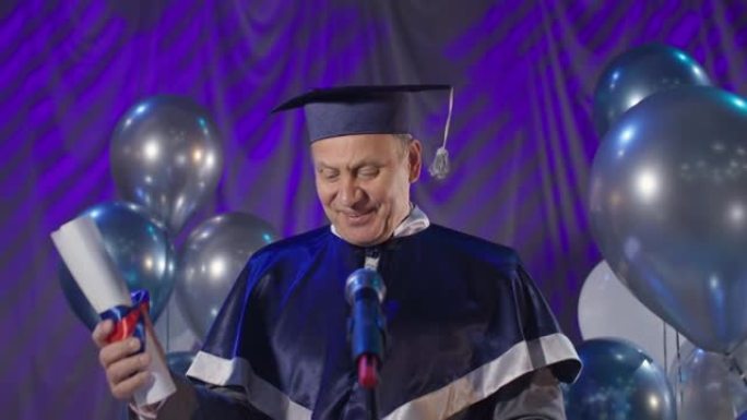 向毕业生颁发文凭，戴着学术帽子和斗篷的男校长祝贺大学毕业的学生，站在气球的会议厅背景下对着麦克风讲话