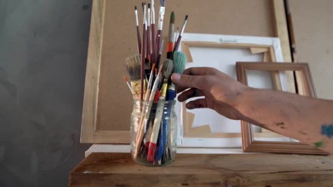 在艺术作坊的架子上的玻璃罐里有画笔，男人和女人的手拿着它们。