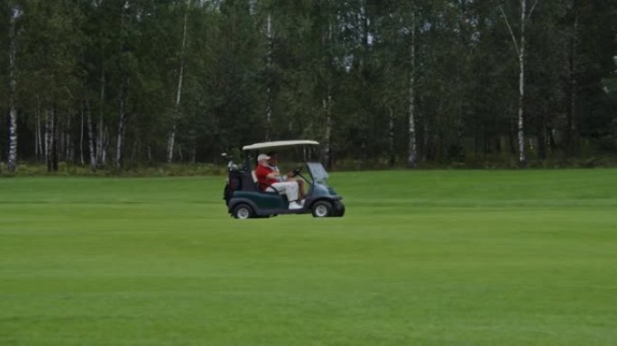 带两名男子和设备的高尔夫球车驶过高尔夫球场的侧视图