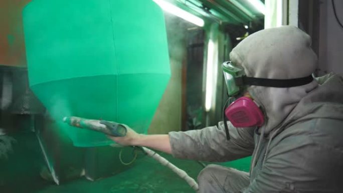 油漆工在特殊的展位上喷涂绿色油漆。在工业制造业工作的安全磨损技术员。工厂室内的喷漆工艺。人在生产中绘