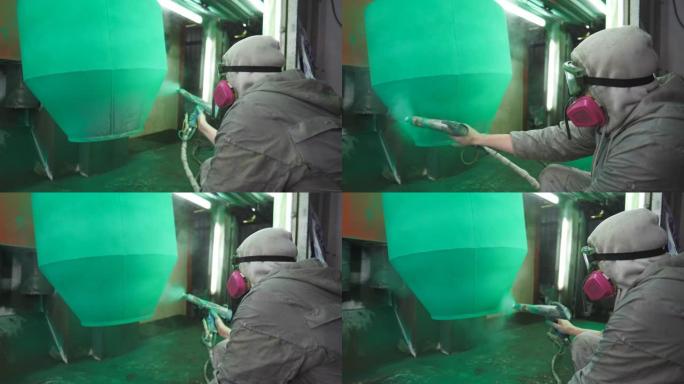 油漆工在特殊的展位上喷涂绿色油漆。在工业制造业工作的安全磨损技术员。工厂室内的喷漆工艺。人在生产中绘