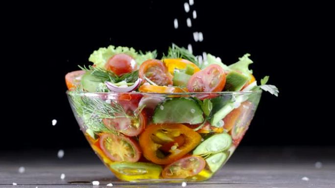 新鲜蔬菜沙拉放在黑色背景的玻璃碗中，撒上粗海盐。黑魔法Ursa Pro G2，4K，150 fps。