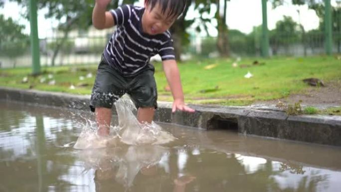 蹒跚学步的男孩在村庄的道路上跳水坑