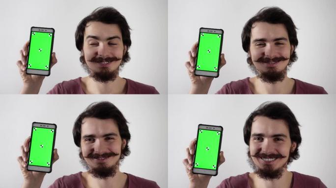 微笑的男人拿着带有绿屏和跟踪标记的智能手机，并在上面显示