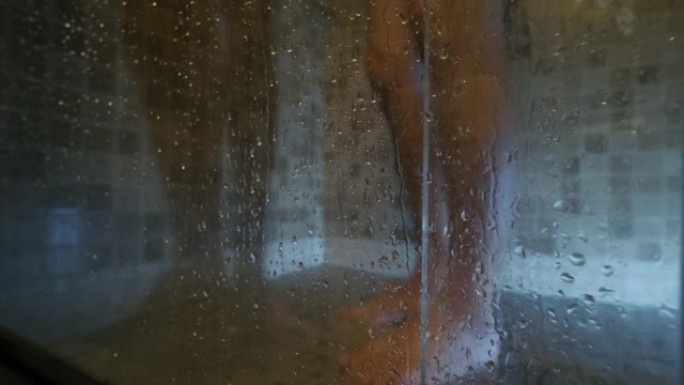 脚在瓷砖玻璃后面的淋浴里。瀑布，玻璃出汗，特写镜头，慢动作。