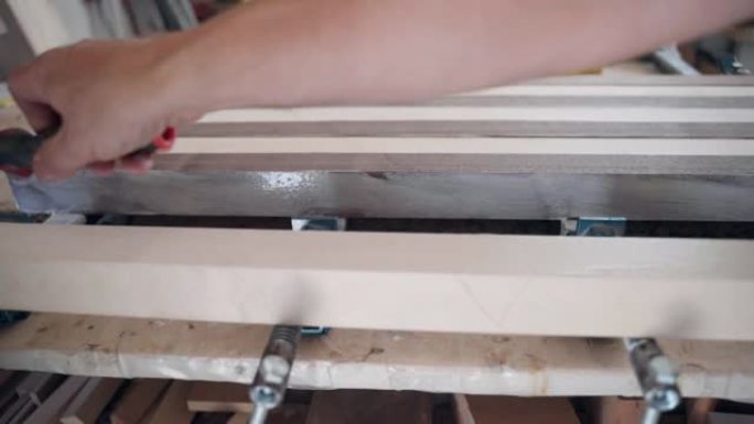 工人使用小压板在木条上涂胶，工匠准备生木条进行涂胶，并制作两种颜色的实心木板。车间木材加工的工业过程
