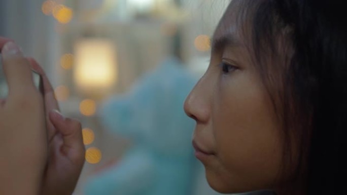 亚洲女孩在家里的夜晚，通过智能手机在沙发上看电影或病毒视频，生活方式概念。