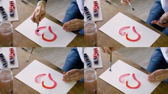 女艺术家的手的特写镜头用水彩画了一颗红色的心。4K