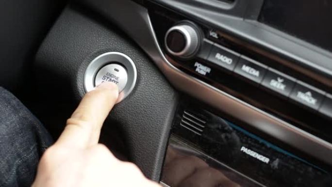 一只男性手指按下车内的启动按钮。