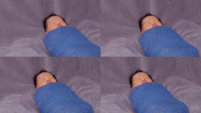 可爱的睡眠新生儿在灰色毯子背景上的蓝色弹力包裹材料中放松。亚洲新生儿婴儿睡眠舒适温暖。新生儿摄影概念