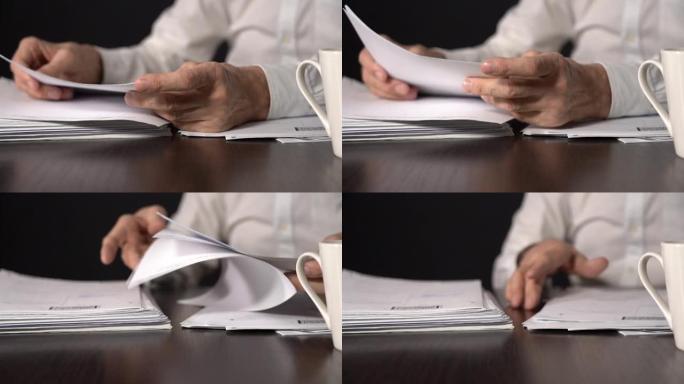 一位上了年纪的办公室职员的手和桌上的一叠商业文件。