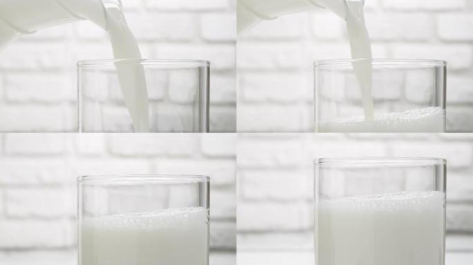 在白色砖墙背景下，将水罐中的牛奶倒入玻璃杯中的特写镜头。奶昔。白色背景上的乳制品