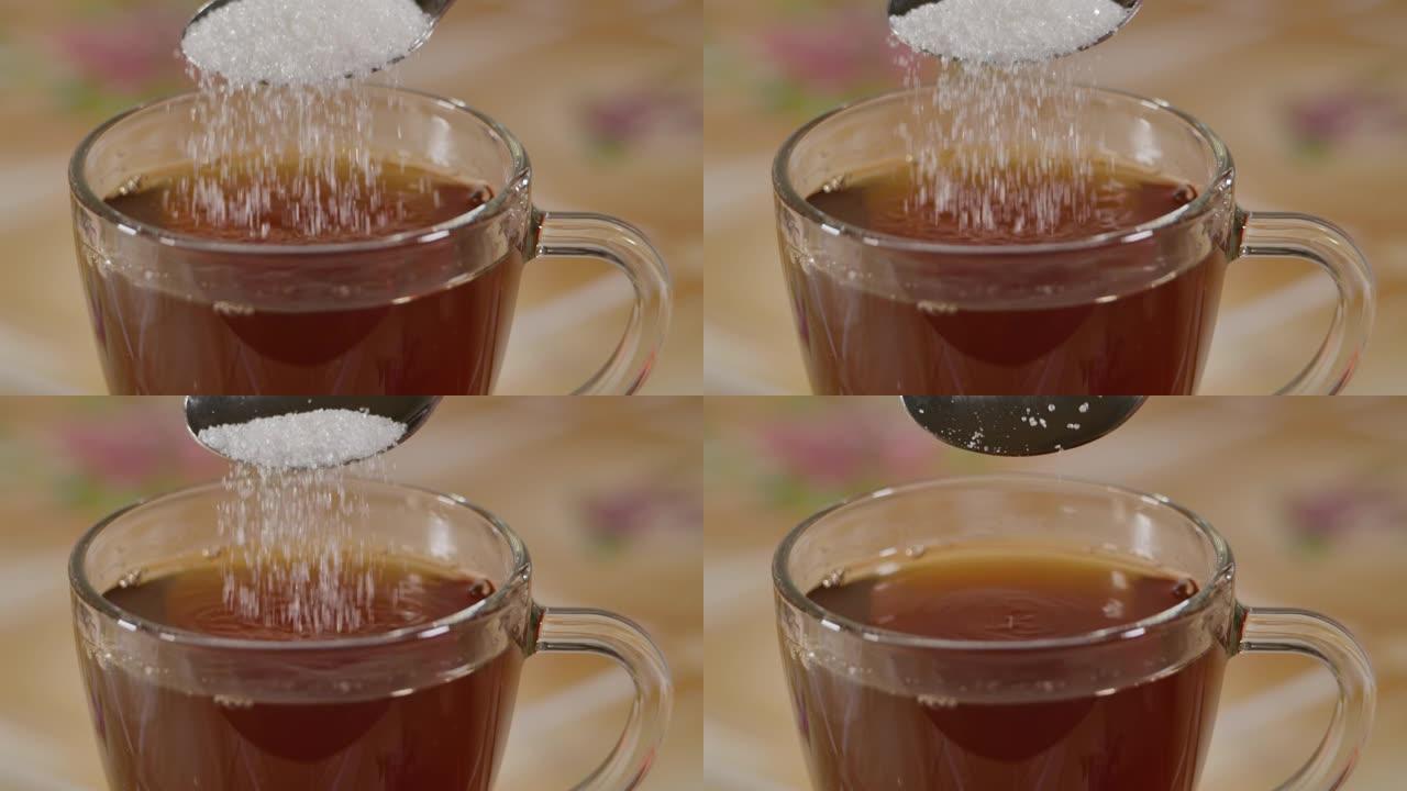 慢动作关闭锁定了从勺子掉入茶杯中的白糖晶体的镜头。倒满汤匙晶体白糖慢动作的特写宏。不健康的饮食，糖尿