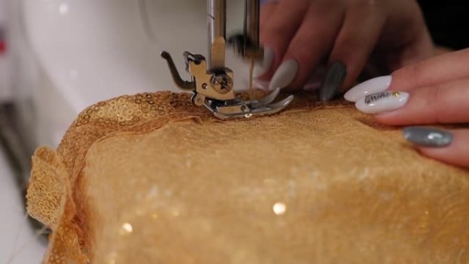 裁缝在缝纫机上缝制由金色镂空织物制成的连衣裙。