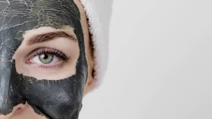 漂亮的年轻女子脸上戴着干粘土泥排毒黑色面具，看着相机