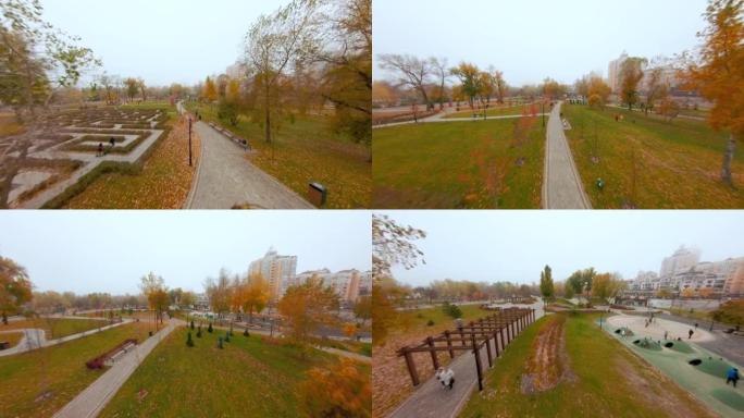 城市公园，人们沿着黄色树叶和景观设计元素的树木之间的小径行走。秋季城市景观