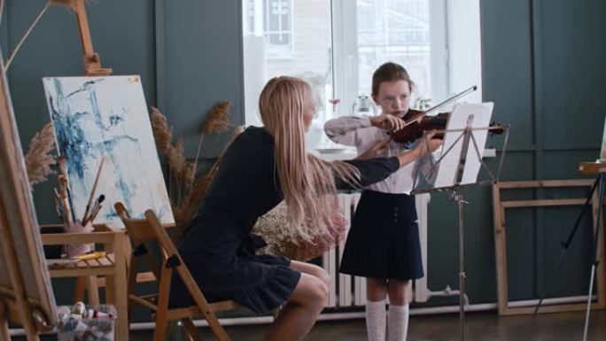 年轻的金发女老师教一个小女孩如何在拉小提琴时正确握弓