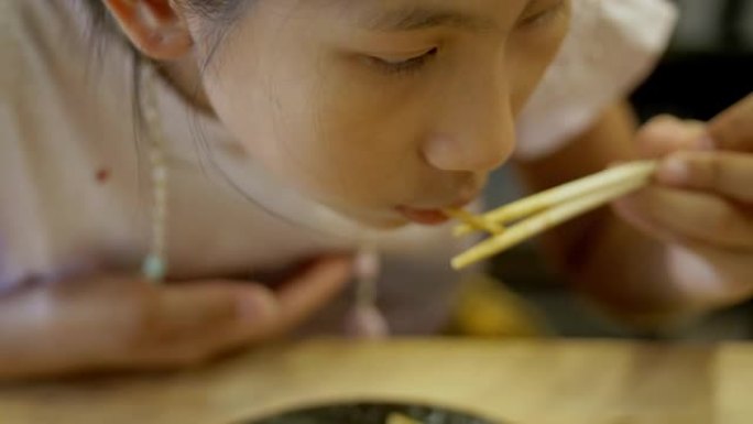 快乐的亚洲女孩和家人一起在日本餐厅享受她的食物，生活方式理念。